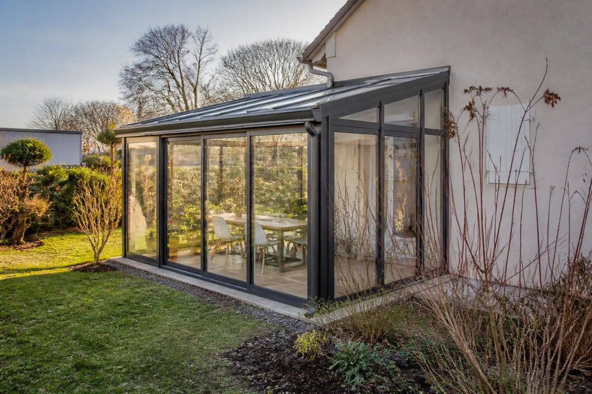 Jardin d’hiver vitré accolé à une maison avec structure en aluminium et végétation hivernale