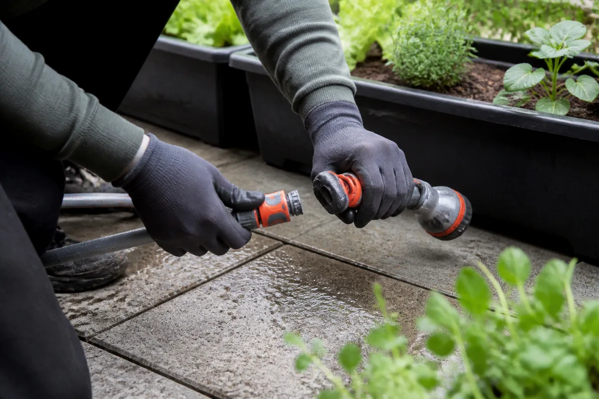Raccord rapide Gardena relié à un tuyau d’arrosage sur une terrasse avec des jardinières