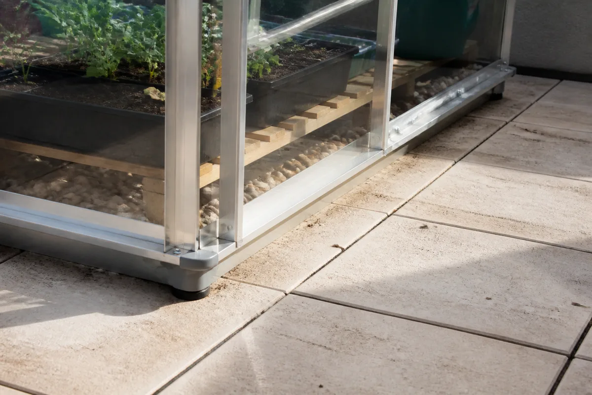 Petite serre en aluminium posée sur une terrasse carrelée sans fondations avec lest réparti et évacuation dégagée